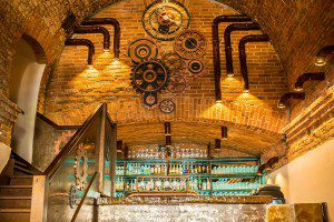 Stylowe lampy miedziane zawieszone nad kontuarem barowym – oświetlenie budujące klimat w lokalu.