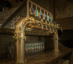 Nalewak do piwa w formie miedzianej bramki z podświetlanymi medalionami LED na nóżkach.